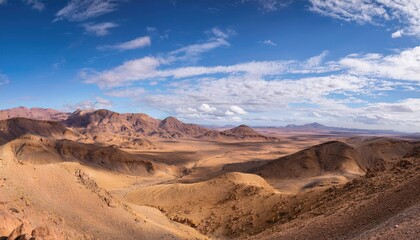 Fototapeta premium Vast desert landscape with mountains under a bright blue sky and scattered clouds. Nature and wilderness concept 