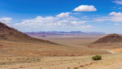 Fototapeta premium Vast desert landscape with mountains under a bright blue sky and scattered clouds. Nature and wilderness concept 