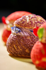 A close-up of an elegant and delicate choux pastry filled with a vibrant purple cream and topped with edible flowers. Selective soft focus