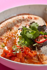 A fresh and vibrant bowl of hummus topped with a medley of colorful vegetables, fresh herbs, and a drizzle of olive oil.