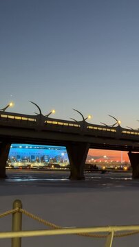 Vertical video showcasing a breathtaking panorama of the ZSD Bridge against a vivid red sunset in St. Petersburg. In the background, the iconic Zenit Arena glows with bright blue lights. 