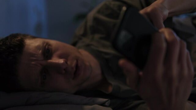 Man lying in bed late at night, glued to his phone, unable to sleep due to overstimulation from digital content and social media.