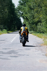 Obraz premium Motorcyclist Riding Down a Peaceful Tree-Lined Rural Road in Daylight..