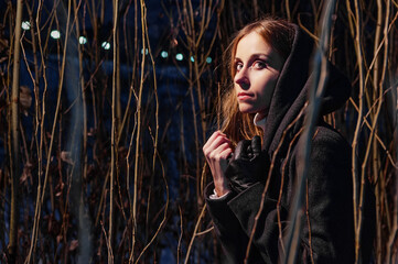 Young Woman in a Dark Hooded Coat Among Leafless Branches..