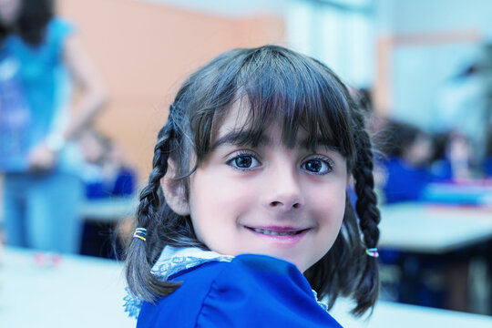 Schoolgirl with forced smile at her classroom desk