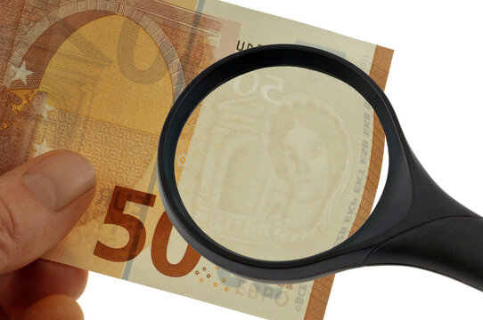 Contr&ocirc;le du filigrane d'un billet de cinquante euros tenu en main avec une loupe en gros plan sur fond blanc