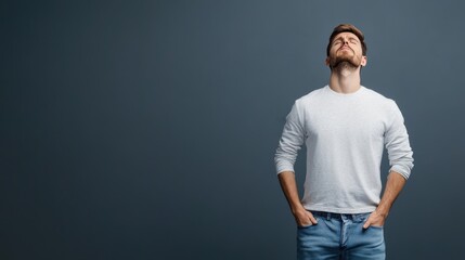 Fototapeta premium Man in Casual Attire Gazing Upward with A Thoughtful Expression Against a Simple Gray Background