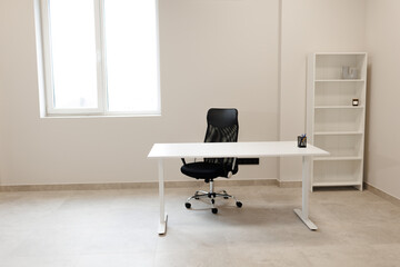 Minimalist modern interior design. Empty office room with white walls and window. Workplace with desk for work, computer table, rolling chair and shelf for document, copy space. Comfortable workspace