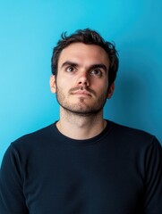 Obraz premium Serious minded man pondering in front of vibrant blue background with large empty copyspace for text, portrait captured from a slightly low angle, focused expression.