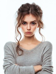 Young woman with serious expression in soft gray sweater on white background, arms crossed, studio lighting, ample copy space for text, emotional tension.