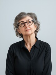 Fototapeta premium Portrait of introspective senior Russian female teacher aged 67 wearing glasses against soft gray background featuring ample negative space for text placement.