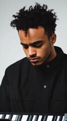Obraz premium Young mixed race male musician concentrating on electric keyboard against neutral gray background with ample empty space for text vertical composition