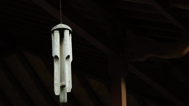 Bamboo wind Chimes hangs on traditional javanese house ceilings or wall against blue sky and agricultural fields backgrounds. Close-up of wooden wind chime in a garden.