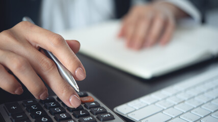 Close up business woman hand using calculator to calculate home finance and writing note,...