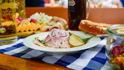 Bayerischer Wurstsalat mit Breze und Spezi im Biergarten auf blau-weißer Tischdecke serviert