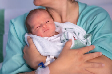 Mom holding a his newborn baby wrapped in a soft blanket, providing comfort and care in a hospital setting after delivery, creating a heartwarming moment of connection between mother and child