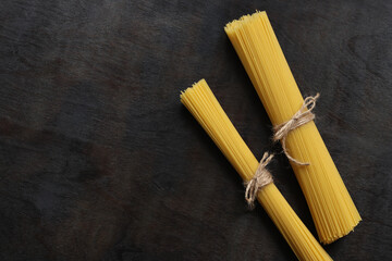Raw dry spaghetti on dark wooden background. Spaghetti from durum wheat. Dry spaghetti tied with thread, top view, copy space. Uncooked yellow pasta. Heap of spaghetti, raw Italian pasta on dark table