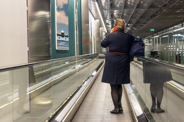 Stewardess is standing on moving walkway at airport and calls from a mobile phone