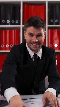 4k UltraHD. Young attractive businessman wearing a suit sitting in armchair throwing euro bills in air. modern office. teal and orange. Vertical Shot.