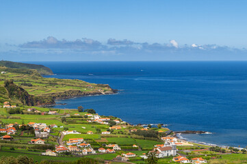 Fototapeta premium Aerial view of Atlantic ocean coastline of Faial Island, Azores, Portugal. White houses, fields, rocks and water. Nature, landscape photography at sunny day.