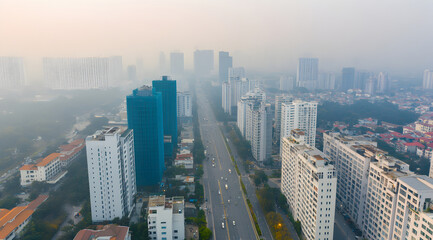 Obraz premium Aerial view of a cityscape shrouded in haze, featuring modern buildings lining a wide road amidst urban development.