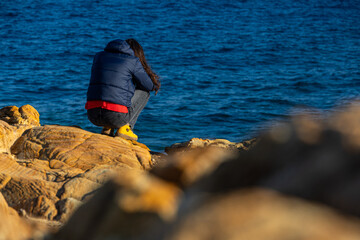 Woman standing alone on the cliffs from an island in the middle of the sea. Concept image for...