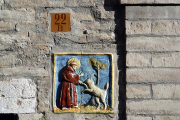 Ceramic tile set into a wall showing Saint Francis befriending a wolf, Assisi, Umbria, Italy