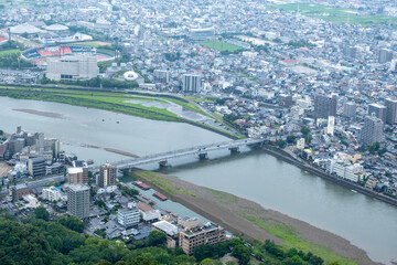 Fototapeta premium A bird's-eye view of a regional Japanese city, Gifu, Japan, shows a sprawling urban landscape with a dense network of roads and buildings along the Nagara River, with a bridge connecting the city. 岐阜市