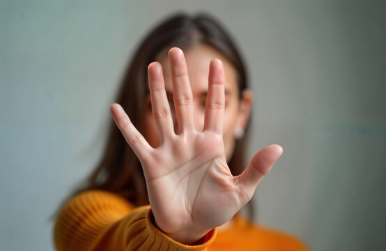Woman displays strong stop gesture. Hand positioned in front of face. Serious expression conveys clear message. Image suggests personal boundaries, privacy. Potentially represents resistance,