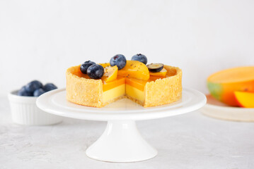 Sliced mango tart with fresh blueberry on a stand on a white table. Sugar, sugar substitutes, lactose and gluten free. Vegan dessert.