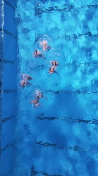 Aerial view of artistic swimming in a clear blue pool. Swimmers perform synchronized movements with splashes and dynamic energy, showcasing grace and teamwork. Perfect for sports, art, and aquatic