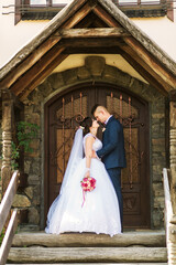 Fototapeta premium A bride and groom are standing in front of a wooden door, with the bride holding a bouquet. Scene is romantic and intimate, as the couple is embracing each other