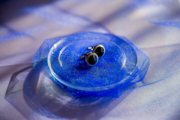 Two earrings, one black and one silver, are placed on a blue plate. The plate is sitting on a blue...