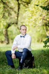 Obraz premium A man wearing a white shirt and blue pants is sitting on a black box in a grassy field
