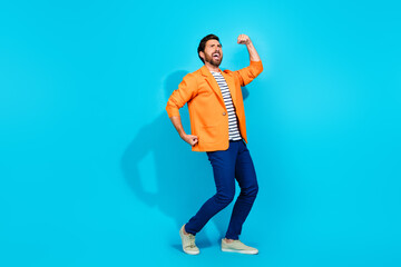 Joyful young man in a bright orange jacket poses dynamically against a vibrant turquoise background