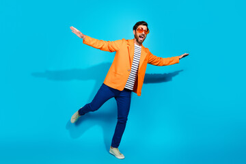 Stylish young man in an orange jacket and striped shirt joyfully posing against a bright teal background