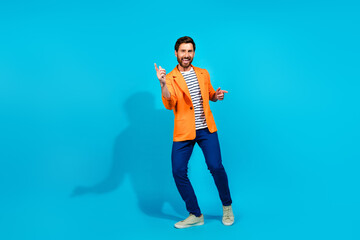 Cheerful young man in vibrant orange jacket posing confidently against a teal background, exuding charisma and style