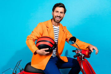 Charismatic young man in vibrant orange jacket holding a helmet, posing confidently on a red scooter against a bright teal background