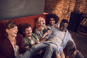 Group of friends laughing and having fun on a couch in bar