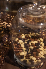 Glass jar with assorted chocolate-covered nuts in a confectionery setting.