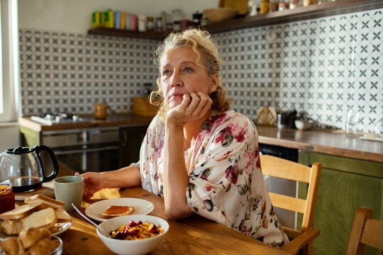 Woman deep in thought at kitchen table with breakfast