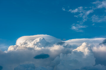 Huge dramatic lenticular cloud on white lush cloudy hill in blue sky. Beautiful cloudscape with big...
