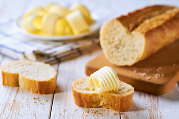 Cut slice baguettes with butter on a light kitchen table.