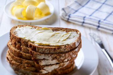 Stack of slices of rye wheat bread with butter, on a light table.