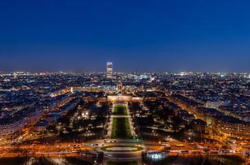 A breathtaking aerial view of Paris at night, showcasing the Eiffel Tower and the illuminated cityscape. The Champs de Mars and surrounding parks are beautifully lit.