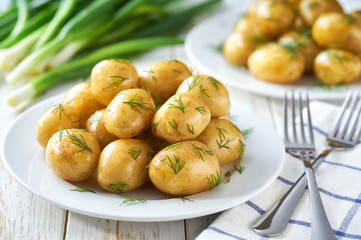 Boiled new or young potatoes with butter, fresh dill and onions in a white plate.