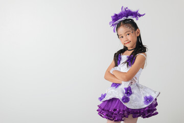 Cheerleader girl in a white and purple dress with a layered skirt, purple feather headpiece, and crossed arms. Studio photo with a clean white backdrop, showcasing her confident pose