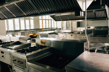 Professional kitchen in modern restaurant displays a shiny metal bowl on stove. Clean arrangement of equipment chrome appliances and new furniture. Bright gas service is working.