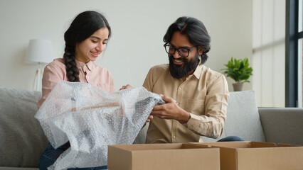 Happy couple customers receive parcel look inside box Arabian Indian man and woman open delivery excited husband and wife shopping online unbox purchase unpacking present make internet order buy goods
