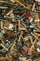 A chaotic pile of assorted screws, bolts, nails, wall plugs, washers, and metal parts. A mix of old and new fasteners in different shapes, sizes, and materials. Close-up shot, workshop tools. 